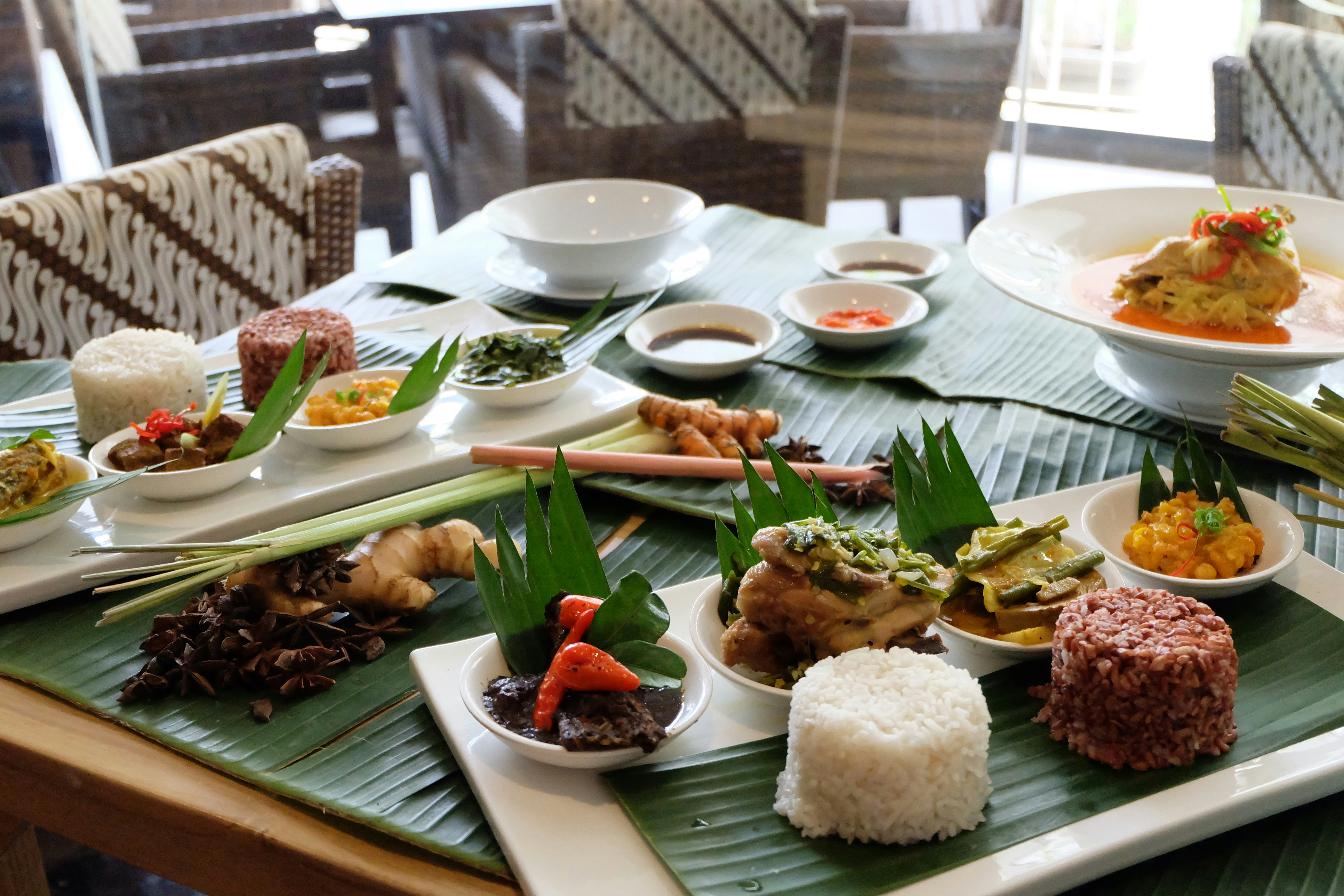 View of a wooden table filled with plates filled with white rice and bowls of small traditional Indonesian food. 